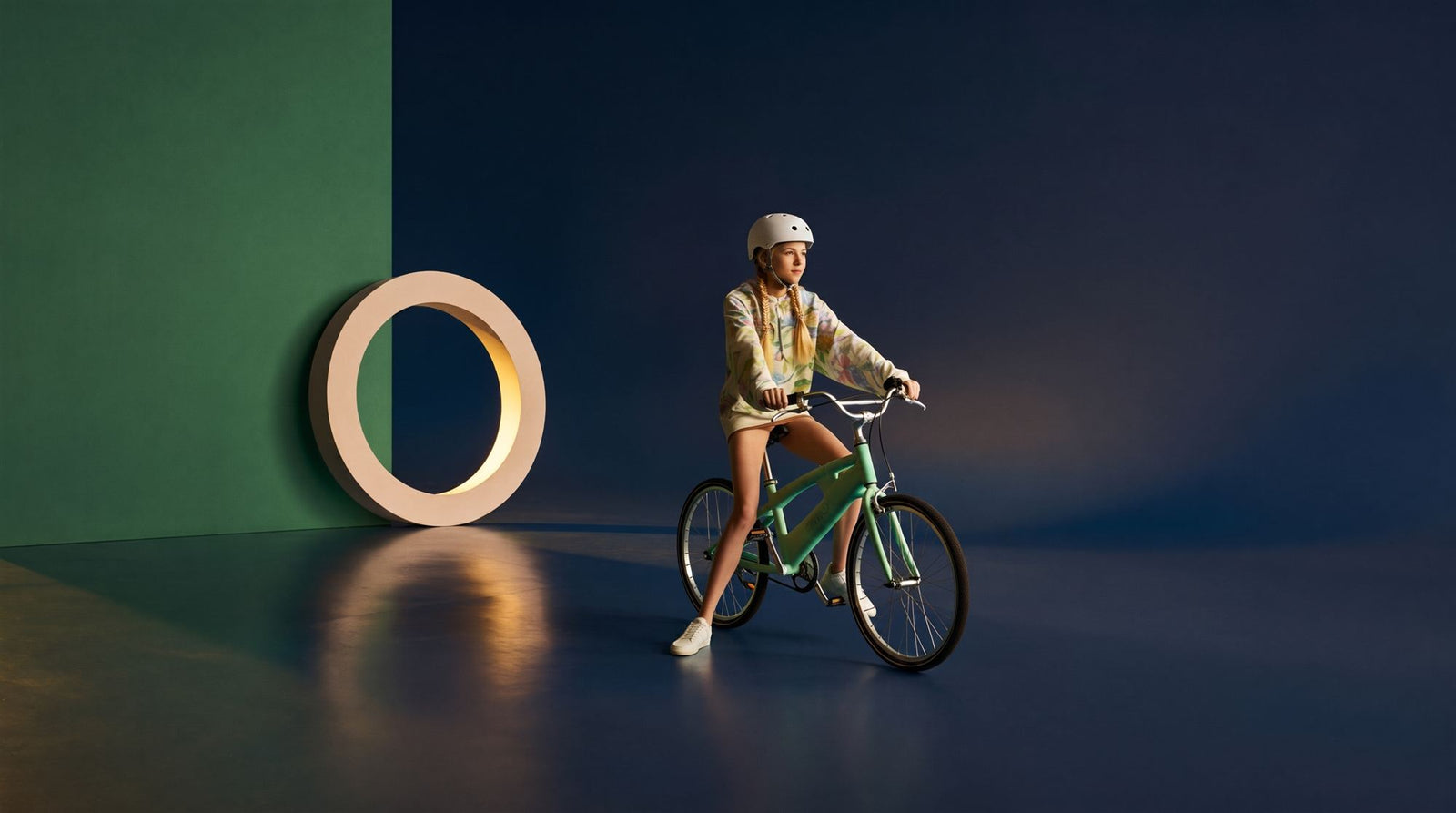 Tiener zit klaar om weg te fietsen op een mintgroene fiets in een donkerblauwe studioset