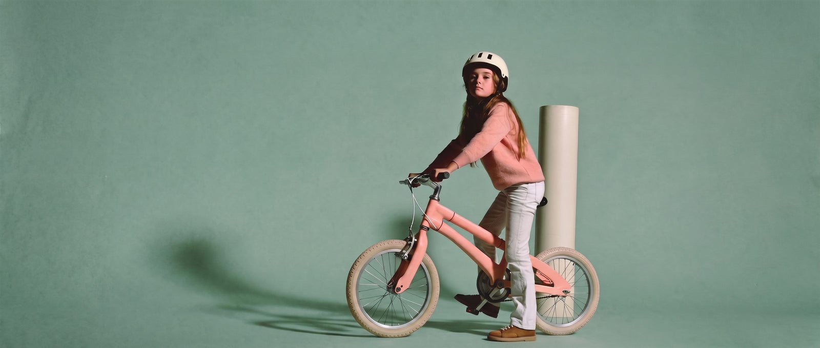 Meisje staat met een roze 22 inch kinderfiets bij een creme zuil in een zachte teal studioset