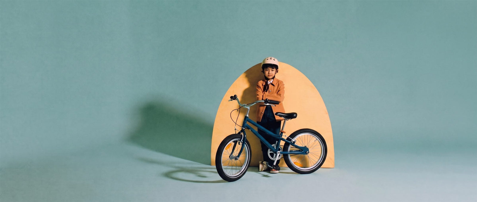 Jongen leunt op een donkerblauwe 24 inch kinderfiets voor een zandkleurige boog in een teal studioset