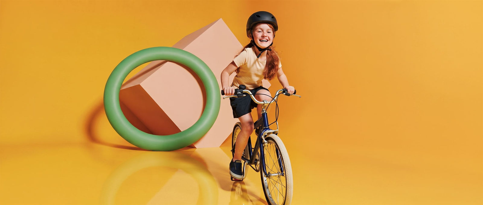 Lachend meisje rijdt op een donkerblauwe kinderfiets door een zonnig gele studioset