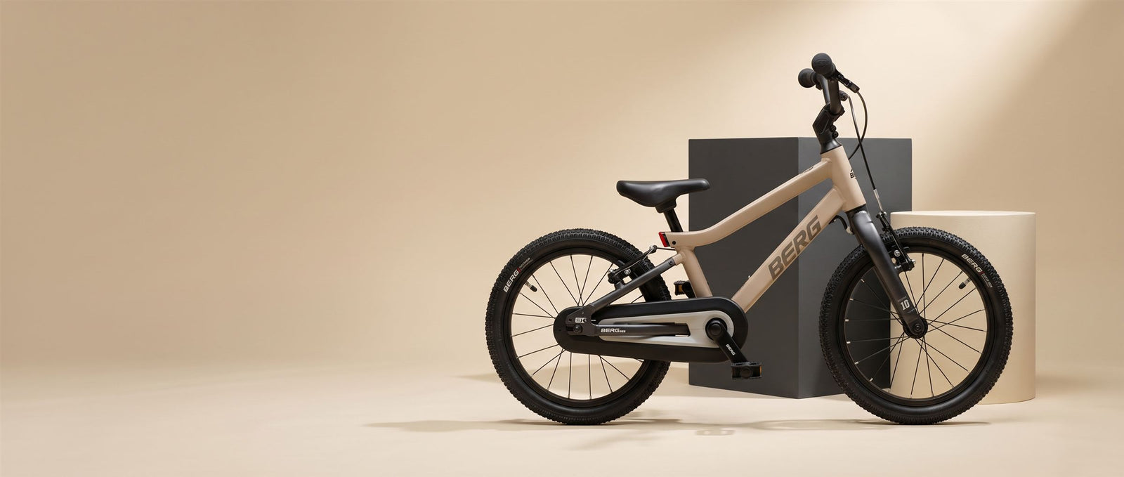 Zandkleurige BERG kinderfiets met zwarte voorvork in een warme zandkleurige studioset