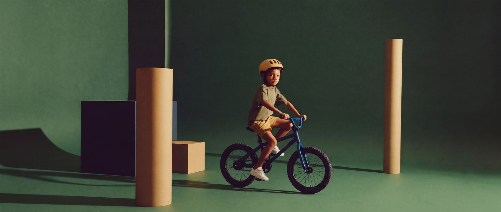 Jongen met gele helm fietst op een blauwe kinderfiets door een diepgroene studioset met zuilen