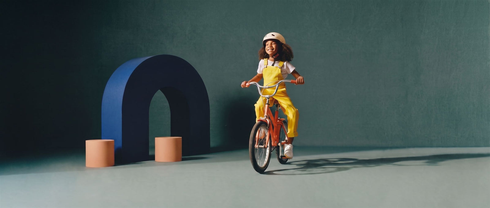 Lachend meisje fietst op een perzikkleurige kinderfiets door een zeegroene studioset met navy boog