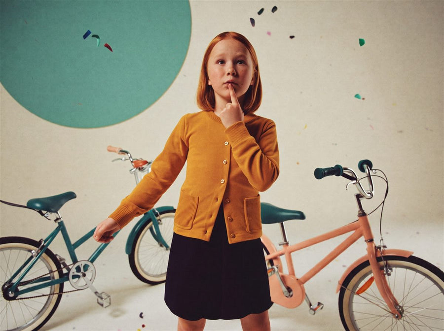 Meisje denkt na tussen twee kinderfietsen in een lichte studio