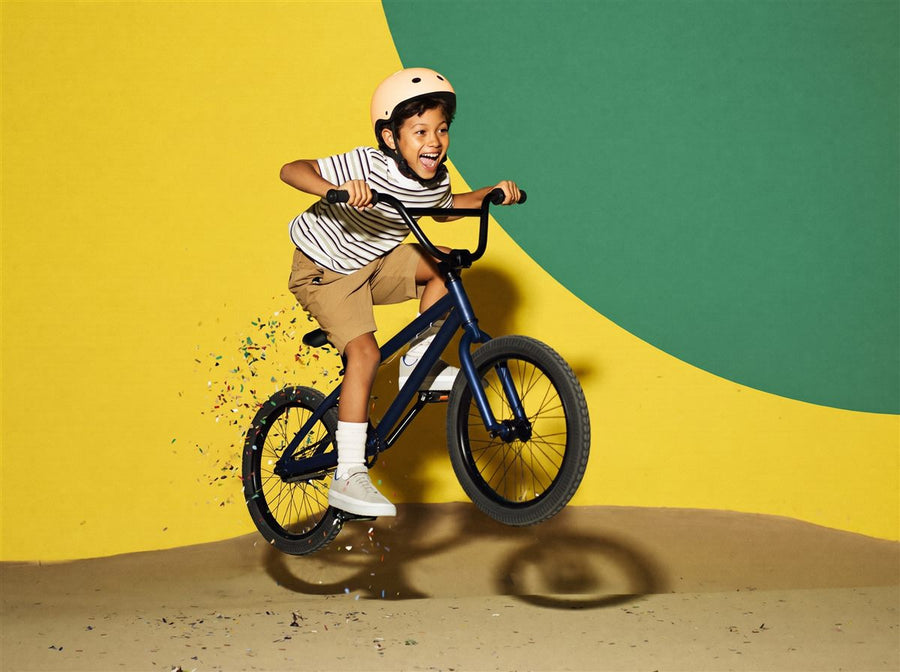 Jongen springt juichend met zijn BMX-fiets door de lucht in een kleurrijke studio