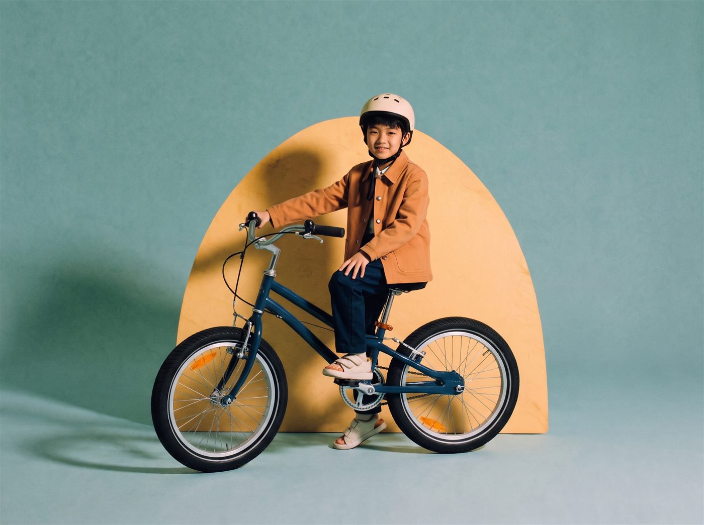 Jongen staat met zijn donkerblauwe 24 inch kinderfiets voor een zandkleurige boog in een teal studioset