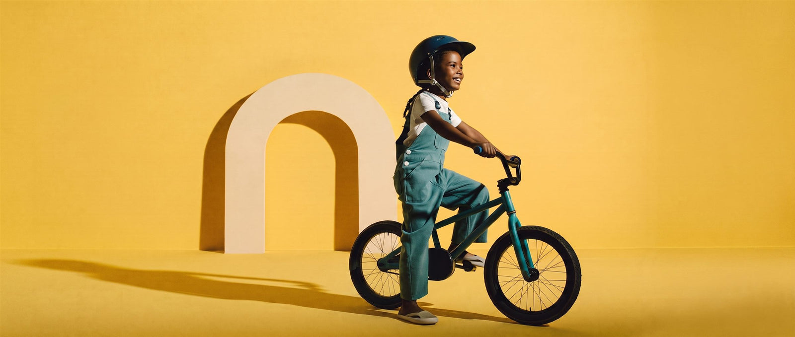 Meisje rijdt lachend op een teal 18 inch kinderfiets voor een creme boog in een zonnig gele studioset