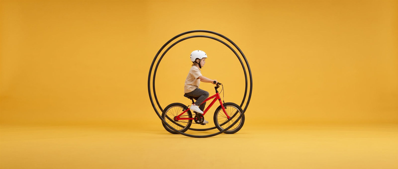 Jongen fietst op een rode 20 inch kinderfiets door grote donkerblauwe ringen in een zonnig gele studioset