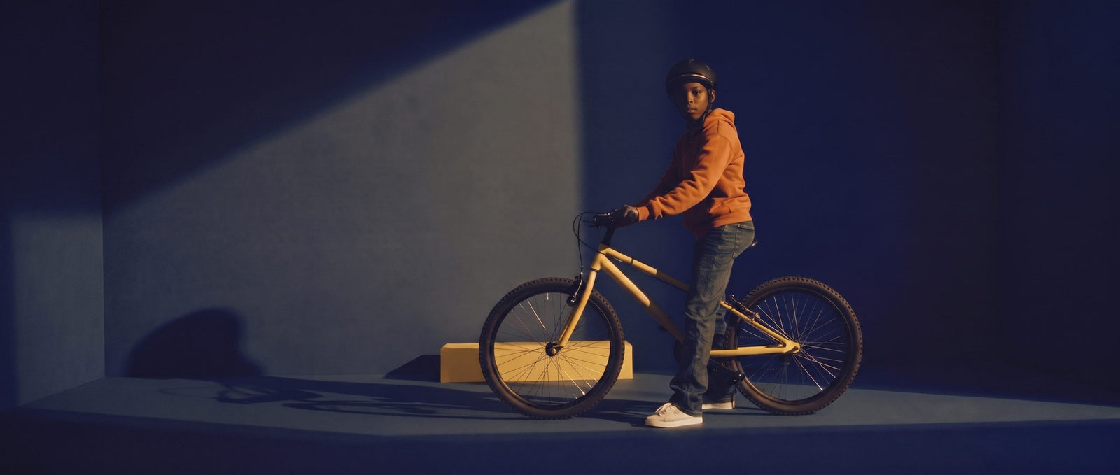 Tiener staat met een zandgele 26 inch fiets in een donkere navy studioset met warme lichtbundel
