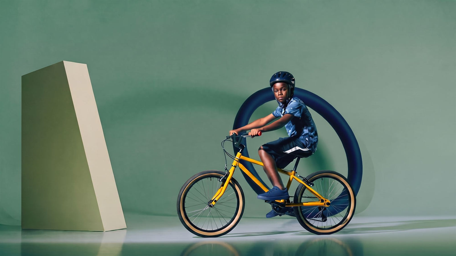 Stoere jongen leunt op een gele kinderfiets in een teal studioset met donkerblauwe ring