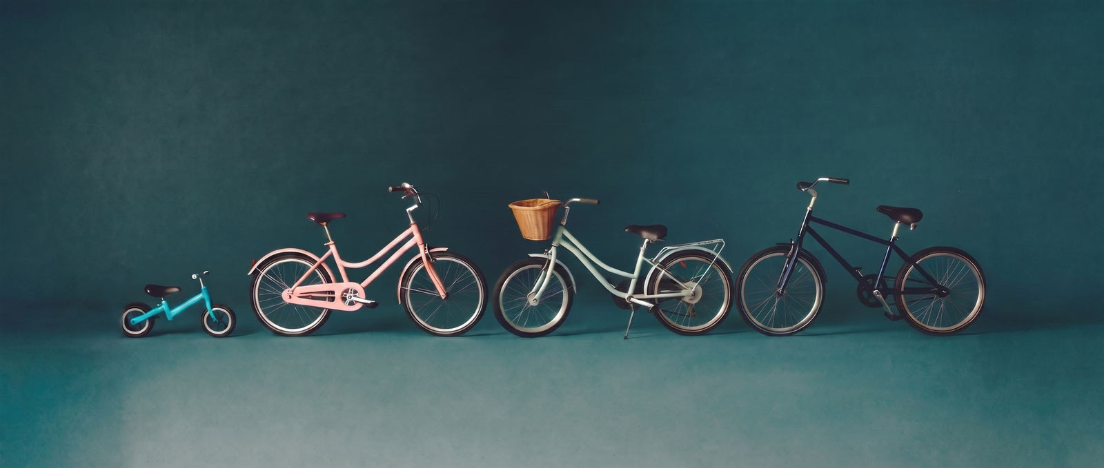 Zes kinderfietsen in vrolijke kleuren op een rij van klein naar groot in een zeegroene studioset