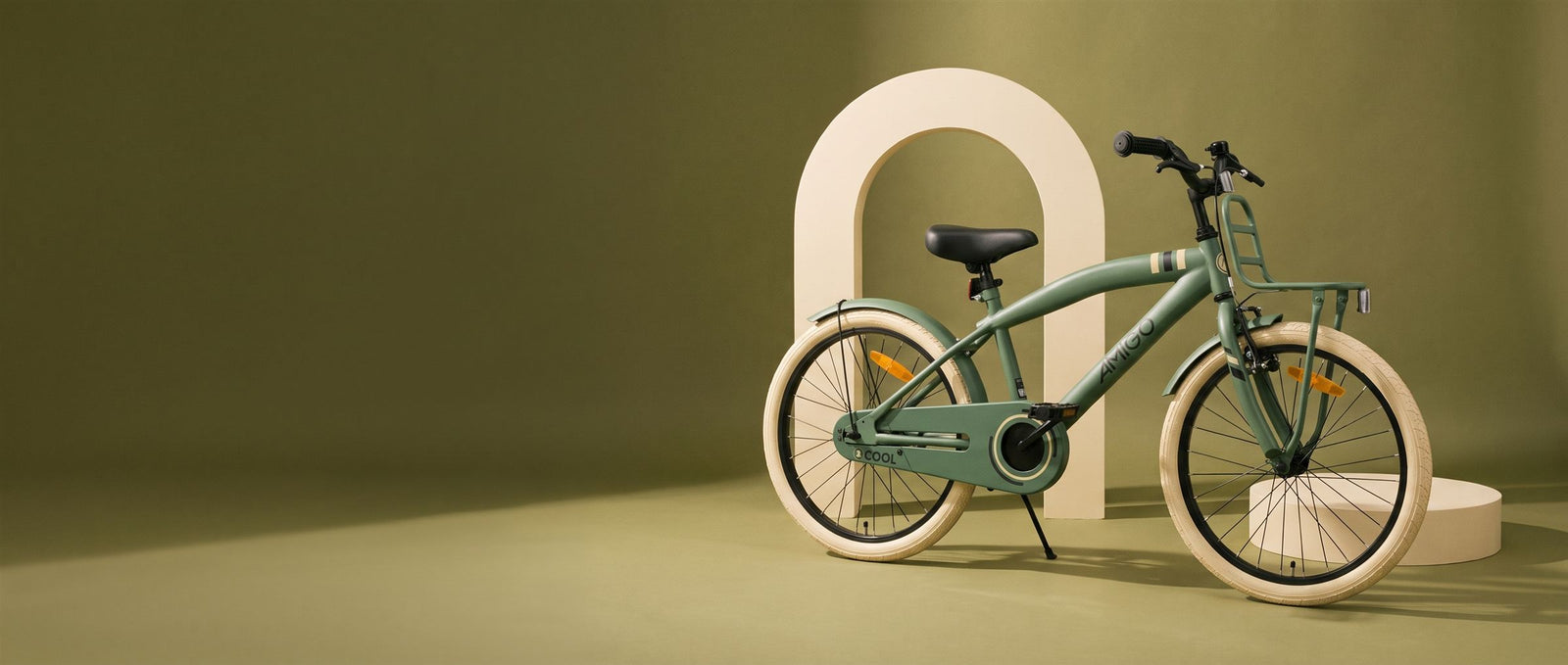 Groene AMIGO kinderfiets met creme banden voor een creme boog in een olijfgroene studioset
