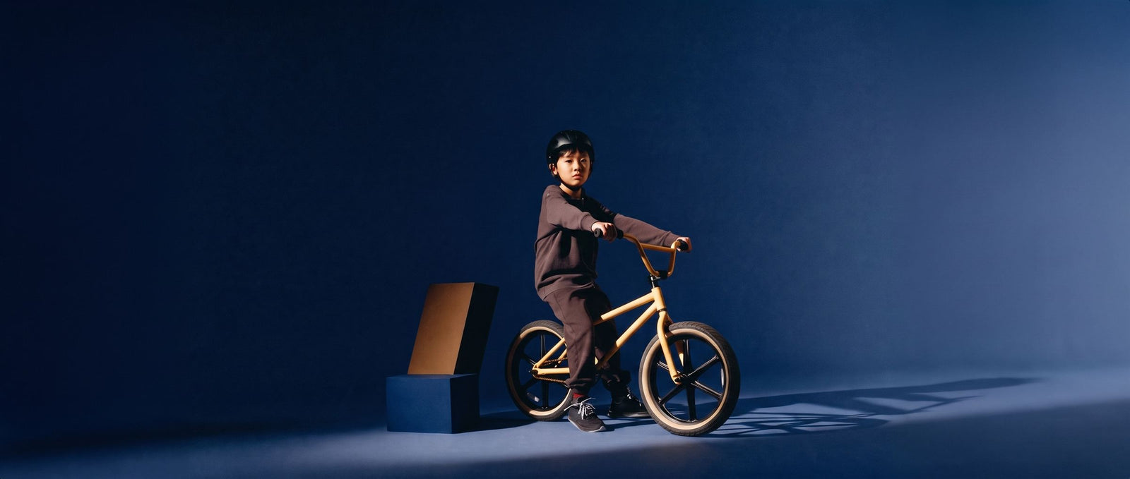 Stoere jongen zit op een zandgele BMX-fiets in een donkere navy studioset met dramatisch licht