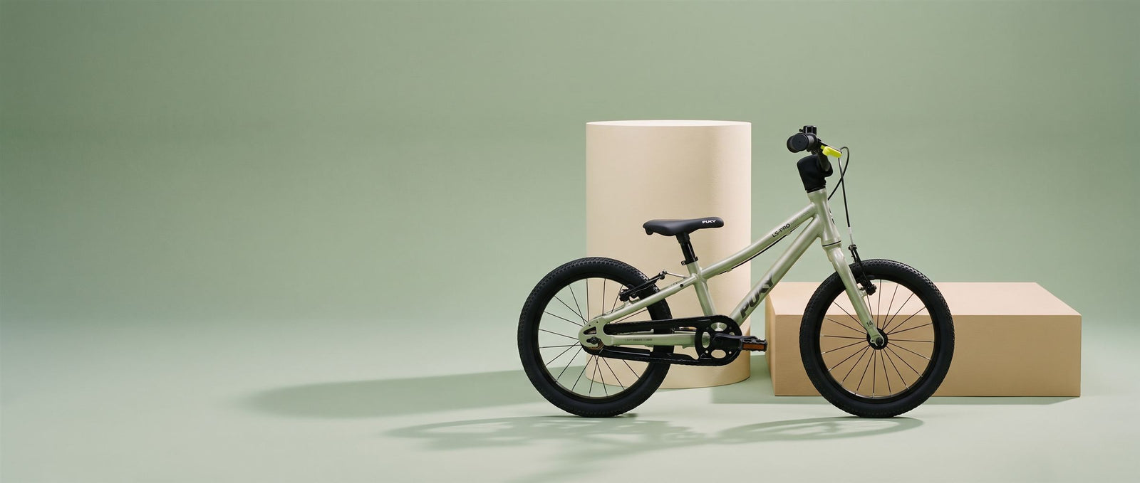 Saliegroene Puky kinderfiets in een rustige saliegroene studioset met creme zuil