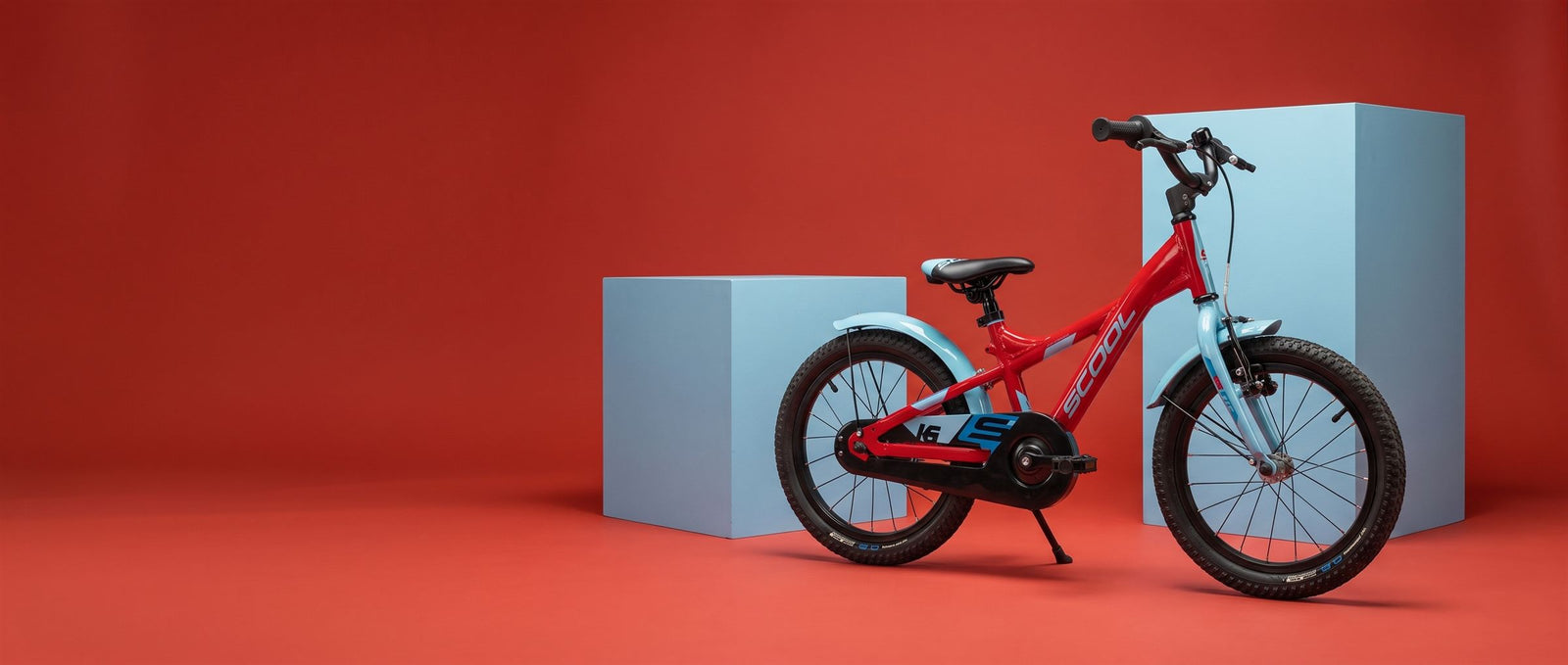 Rode S'COOL kinderfiets met lichtblauwe voorvork in een warmrode studioset