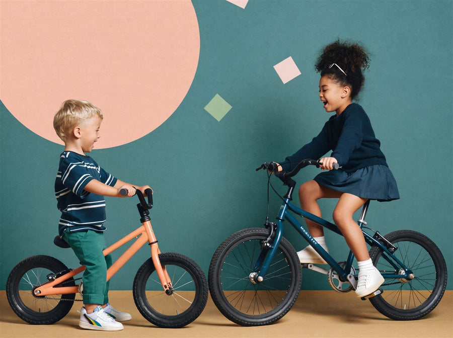 Twee kinderen van verschillende leeftijden lachen naar elkaar op hun eigen maat kinderfiets