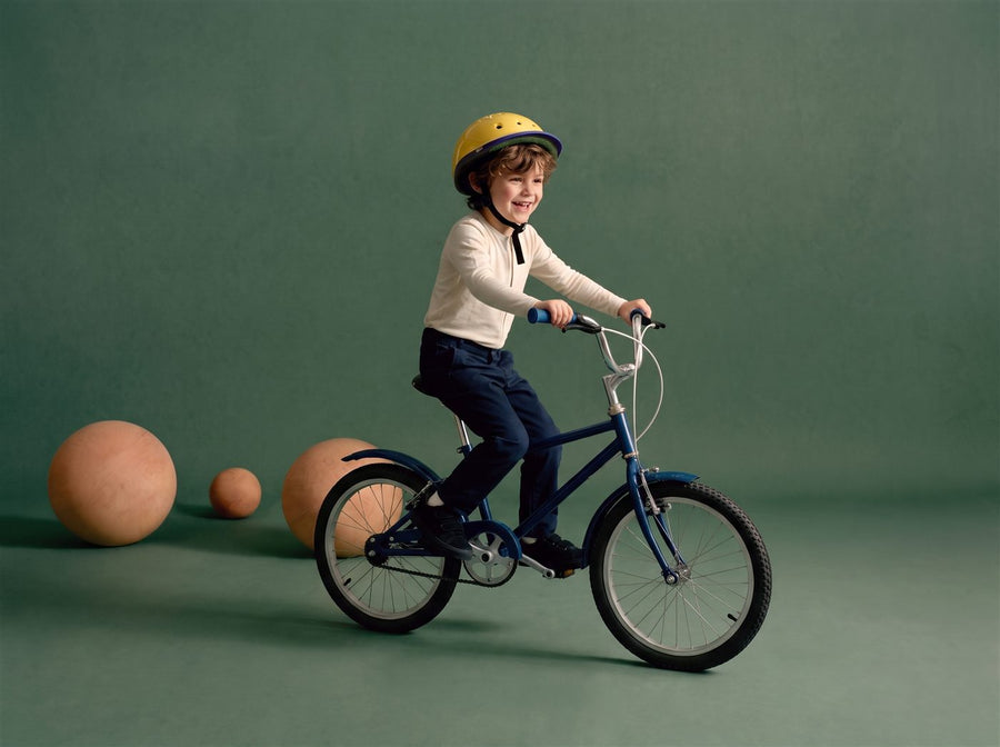 Jongen zit trots op zijn donkerblauwe 16 inch kinderfiets in een zeegroene studioset