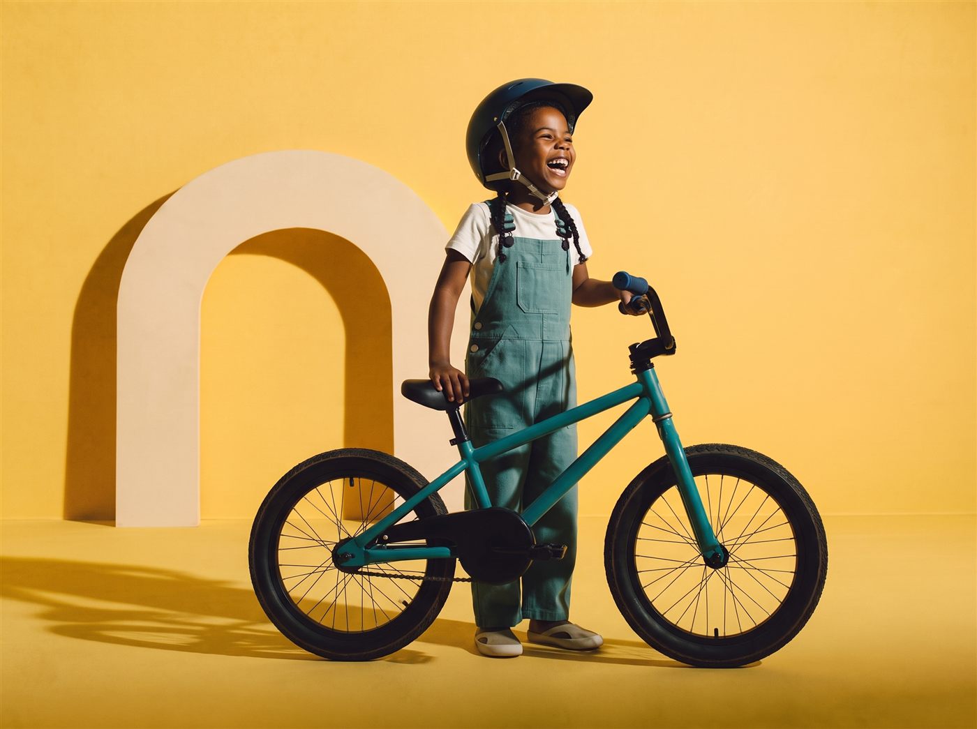 Meisje staat lachend naast haar teal 18 inch kinderfiets in een zonnig gele studioset