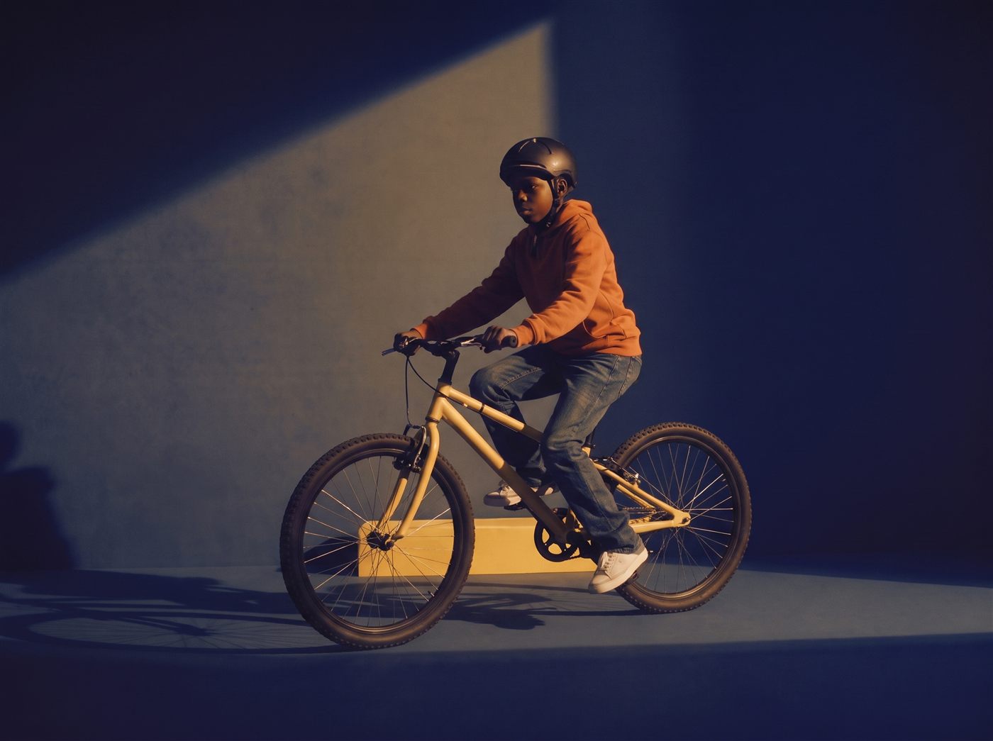 Tiener staat met zijn zandgele 26 inch fiets in een donkere navy studioset met warm licht