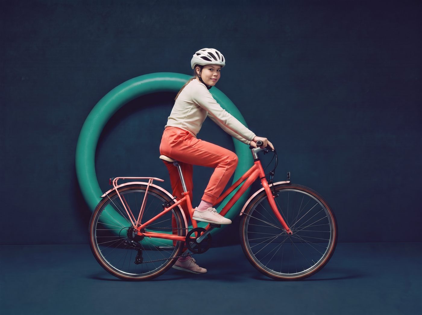 Tiener staat met haar koraalrode 27,5 inch fiets voor een groene ring in een donkere navy studioset