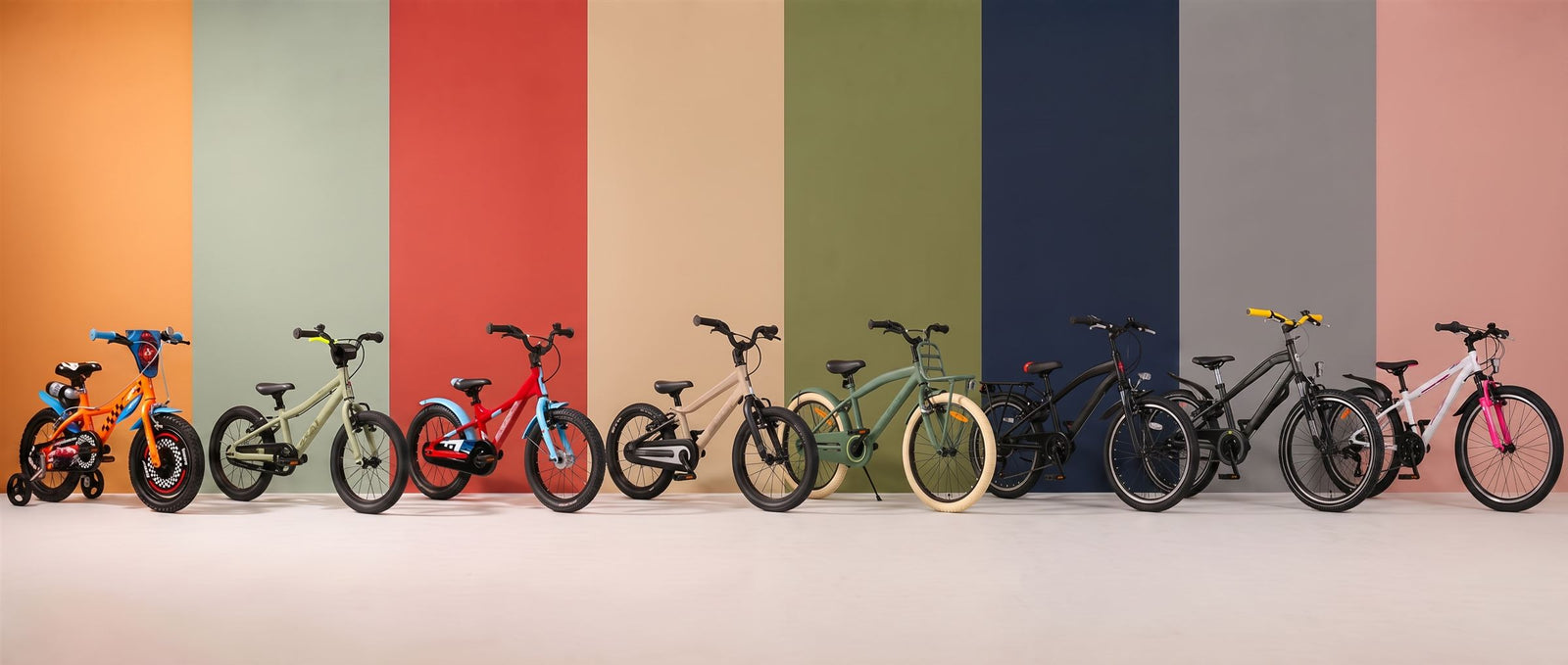 Acht kinderfietsen van onze merken op een rij, elk voor een eigen gekleurde studiobaan