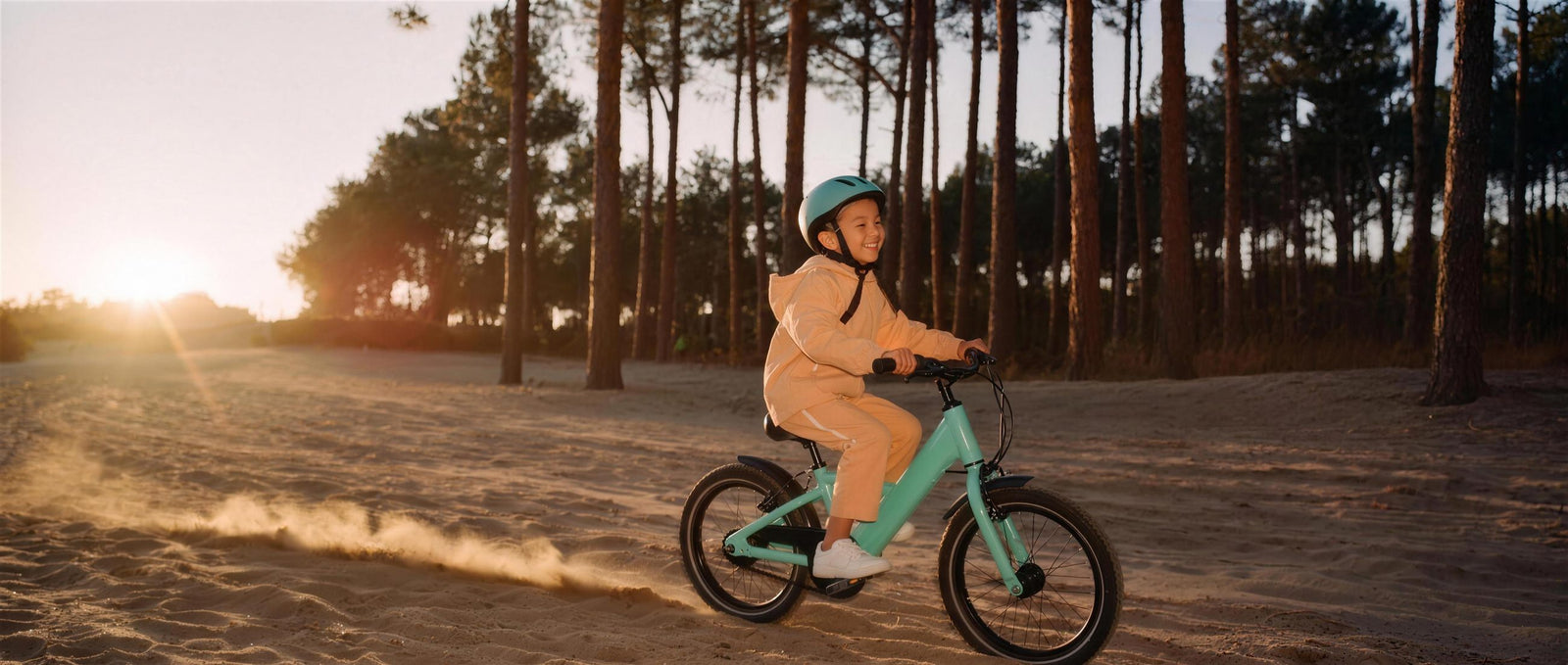 Kind crost op een zeegroene fiets door gouden avondzon over een zandpad, stof stuift op